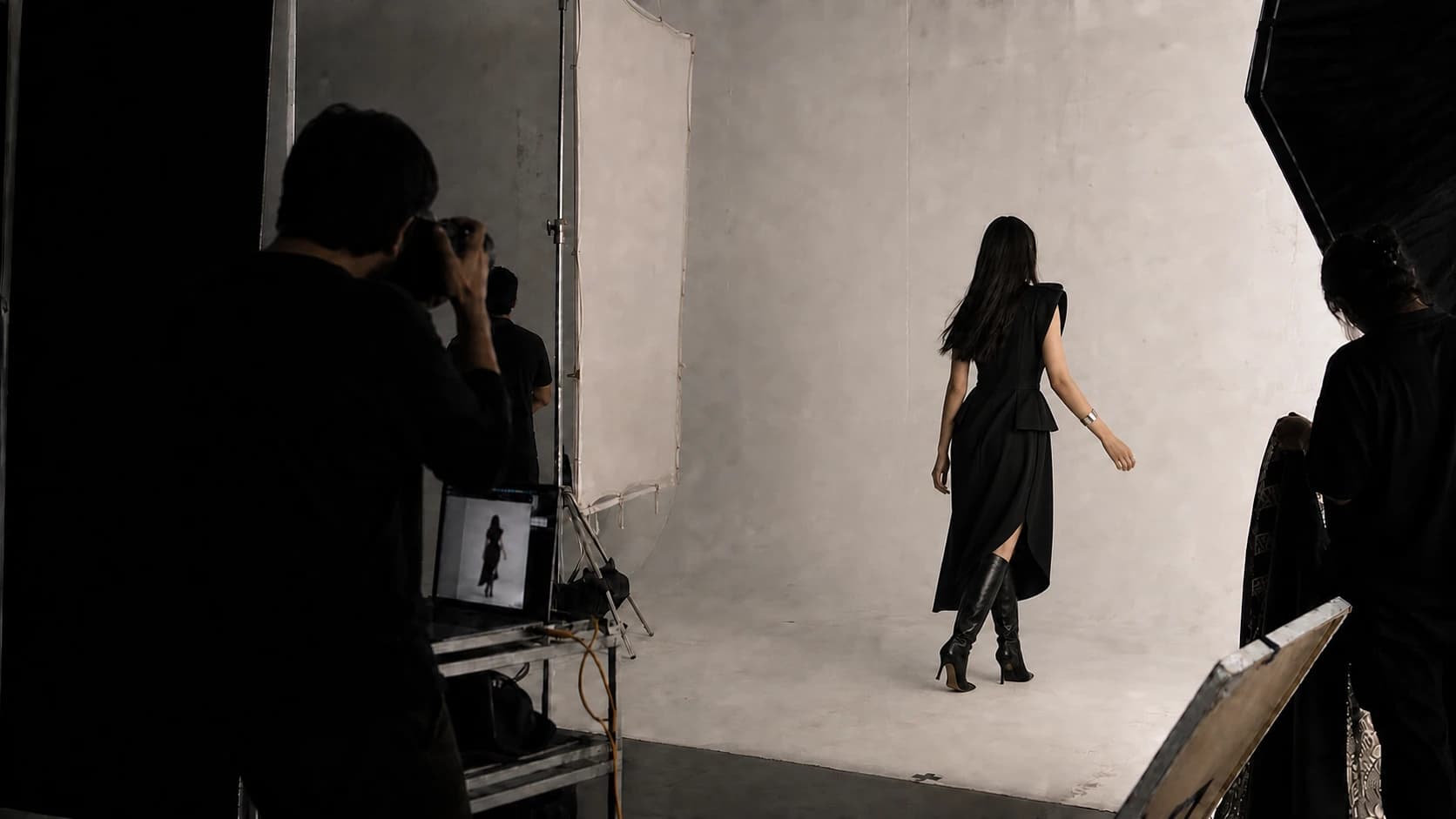 Fashion photographer filming a model from behind on a white studio set